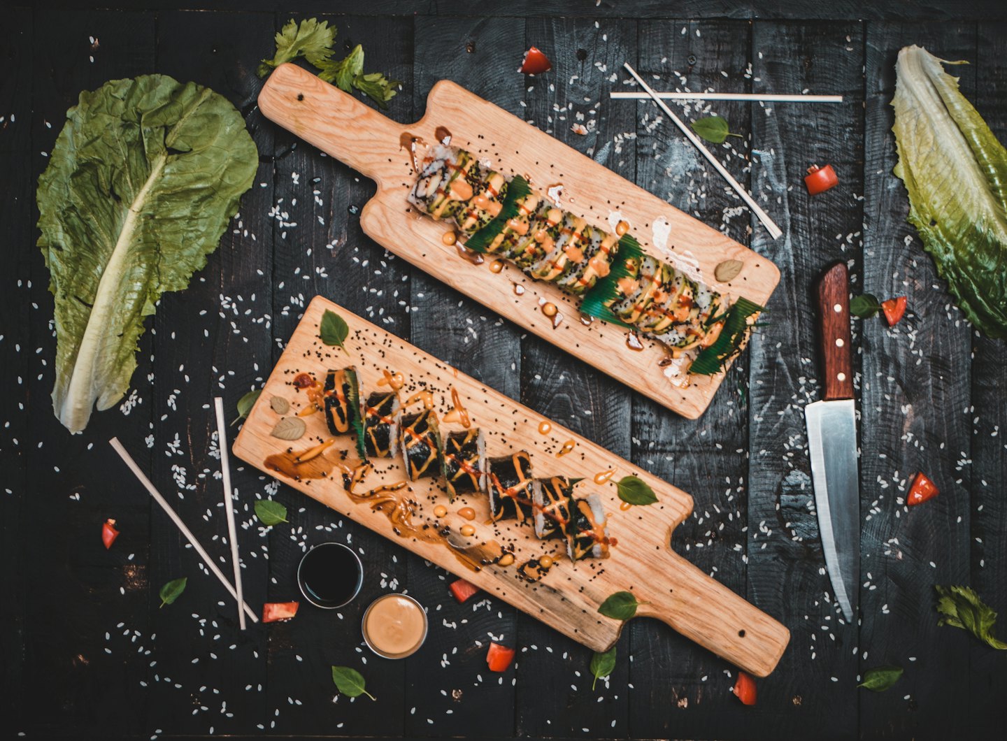 Roladki sushi na drewnianych deskach z kolorowymi sosami i ziołami.
