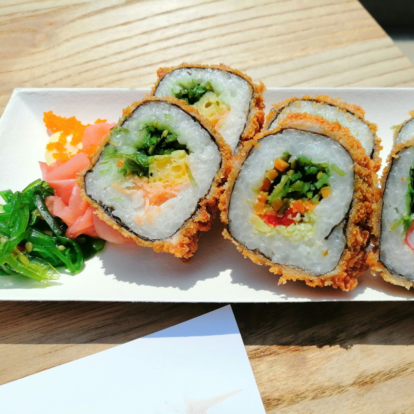 Smażone rolki sushi z sałatką z wodorostów i marynowanym imbirem na drewnianym stole.