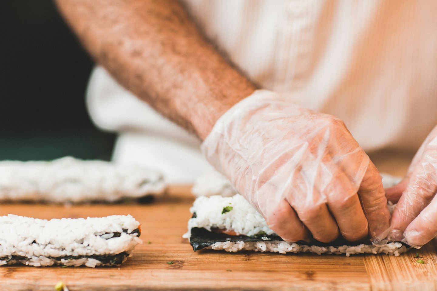Szef kuchni w rękawiczkach przygotowuje sushi na drewnianej desce do krojenia.