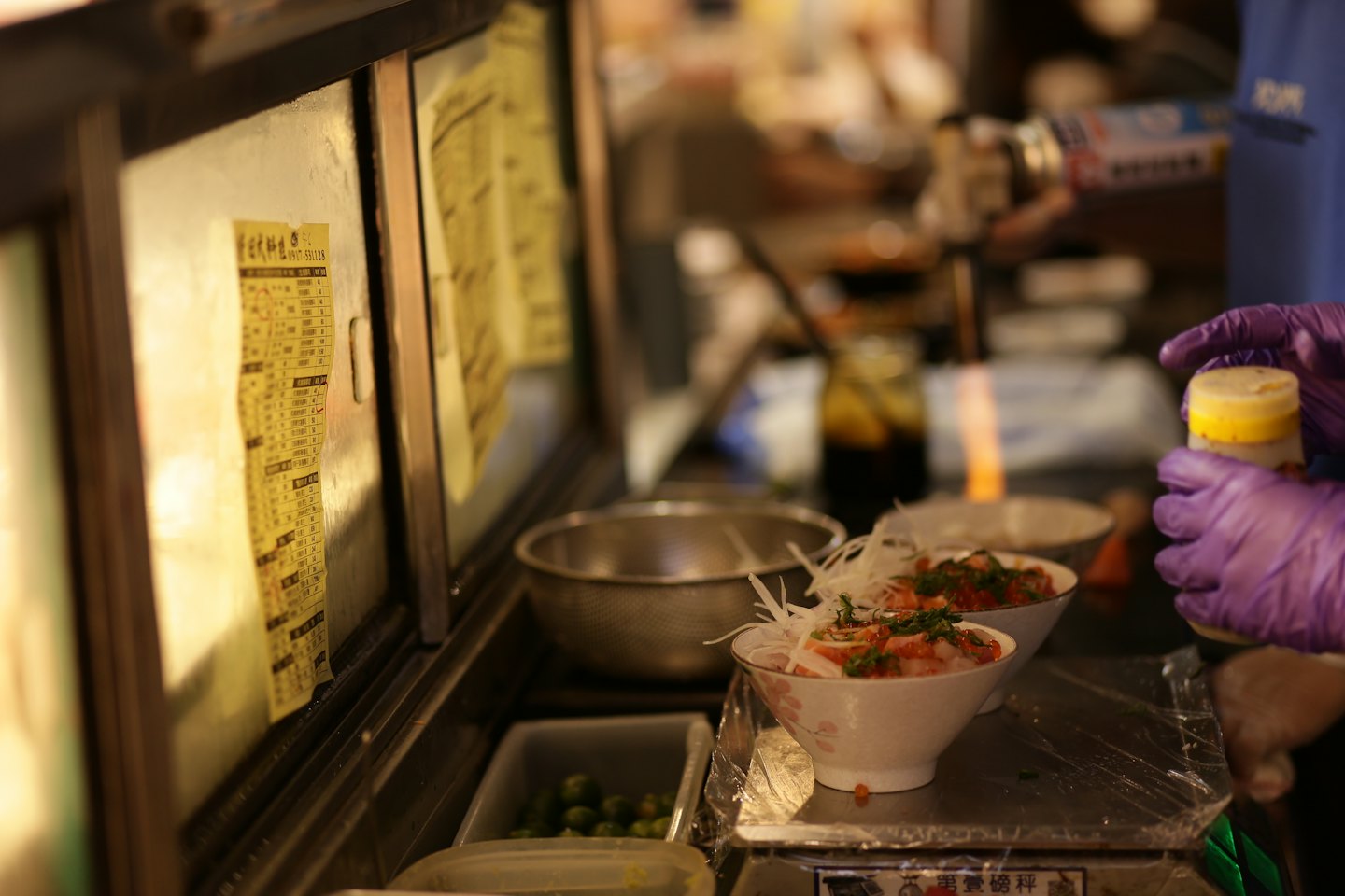 Szef kuchni w fioletowych rękawiczkach przygotowuje miski z dodatkami do sushi.