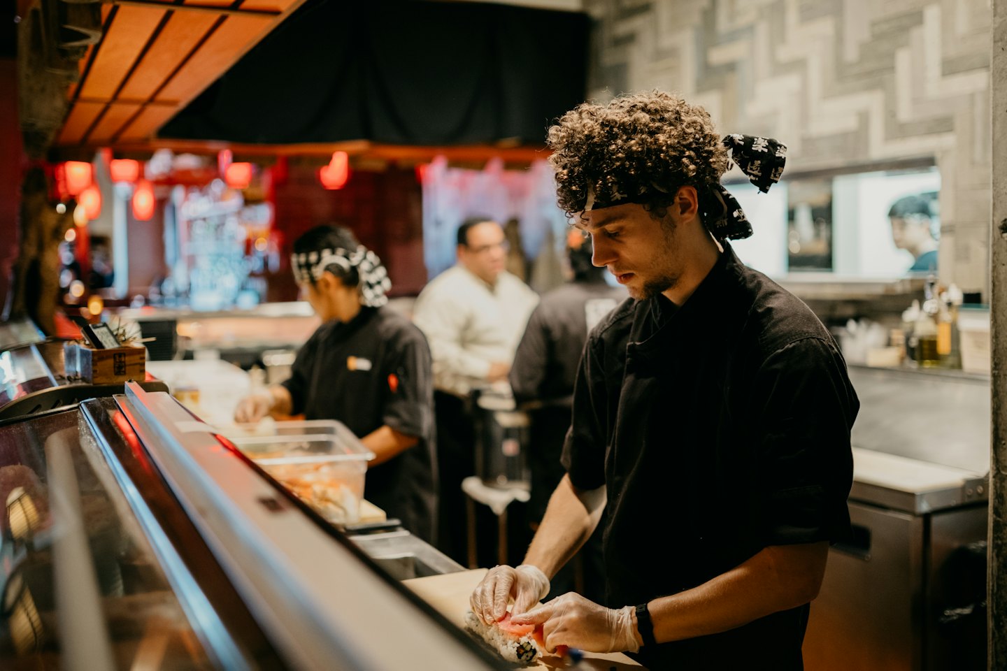 Szef kuchni sushi w rękawiczkach zwija rolkę sushi w kuchni restauracji.